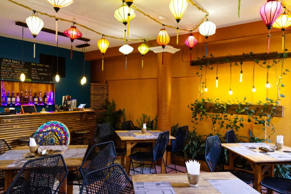 Colorful Asian lanterns hang from the ceiling of Chili Garden, the best Asian restaurant in Puerto Escondido. Below are tables and chairs in front of the small bar.