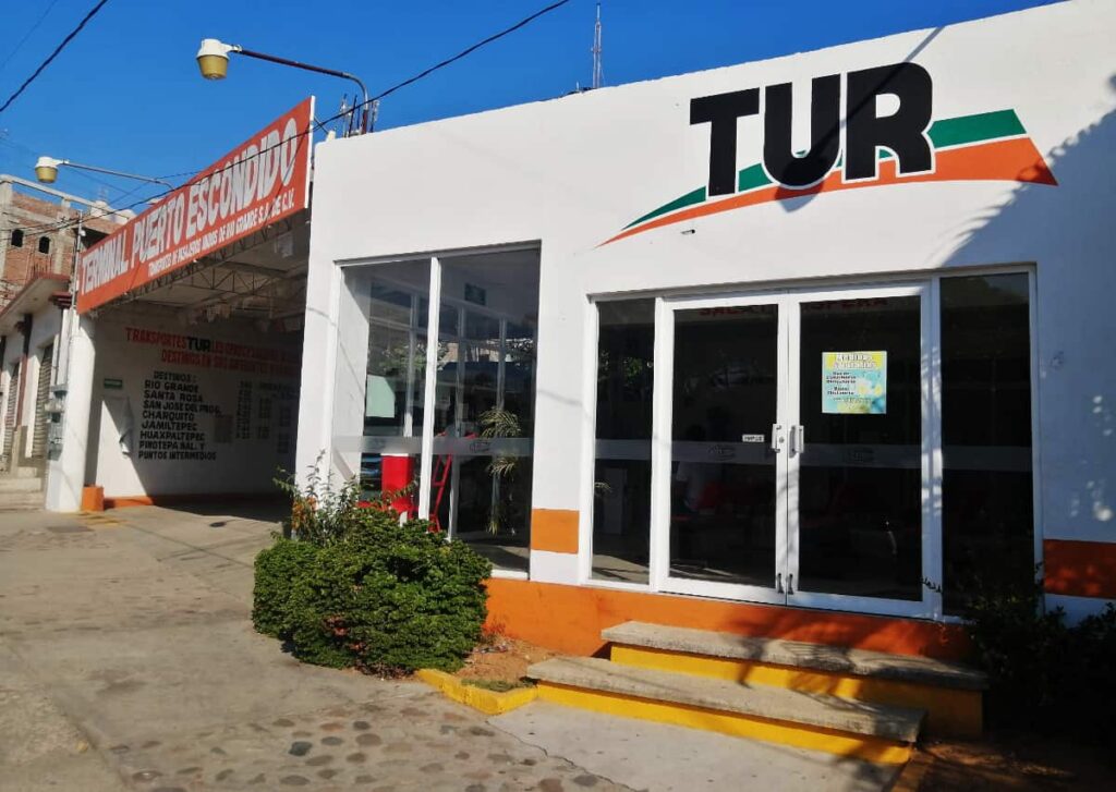This white building houses the colectivo to get to Chacahua from Puerto Escondido. Above the glass doors, the word TUR is painted in black with a green and orange decorative swoosh behind.