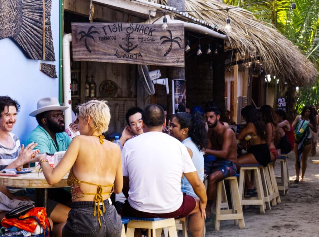 Under a wooden sign that reads, Fish Shack, La Punta, patrons dine at the tables along a corridor that leads to the beach.