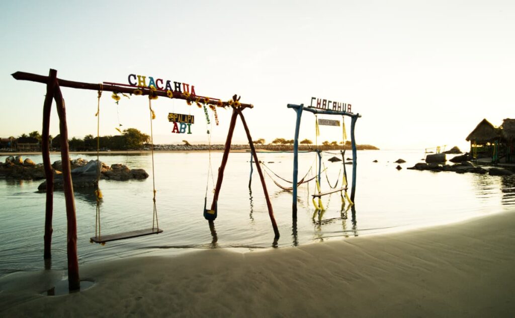 Wooden swing set sit in the shallow Chacahua lagoon. Across the top, colorful letters spell out Chacahua.