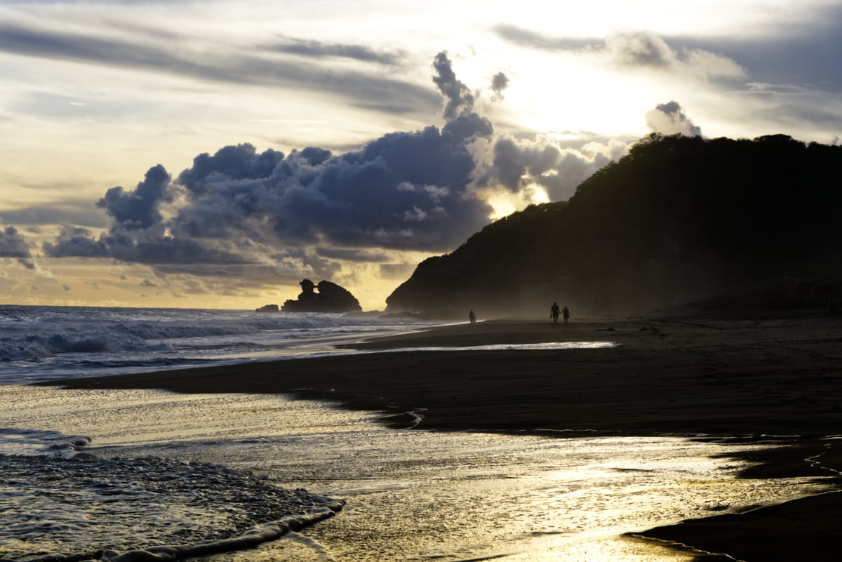 The backlit mountain juts into the sea as the sun streams across the wet sand as the waves retreat from one of the beaches in Mazunte, Oaxaca.