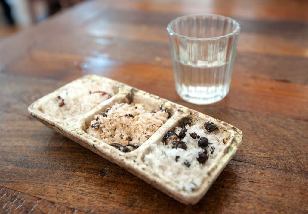 During a mezcal tasting, a shot of mezcal sits in front of a vessel divided with three different salts.