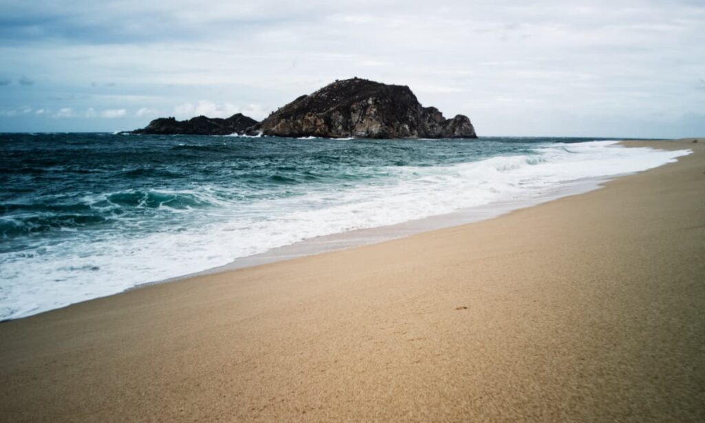 With views of a large rock in the ocean, waves roll in on a stormy day at Cacaluta Beach in Huatulco.
