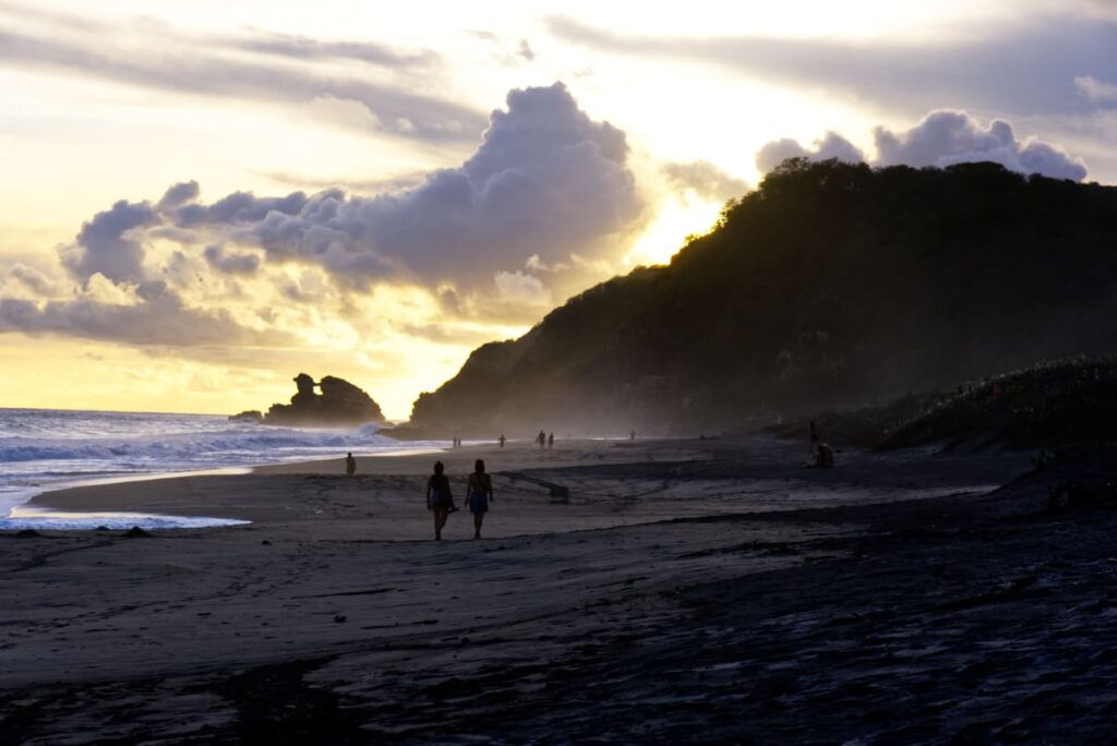 A silhouetted couple walk along the backlit Mermejita Beach as the sun sets in Mazunte.
