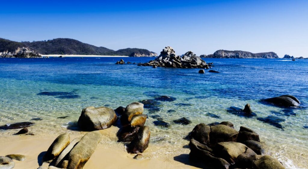 Small rocks in the shallow, blue waters of San Agustin Bay. Larger rock formations can be seen further out, in the ocean.