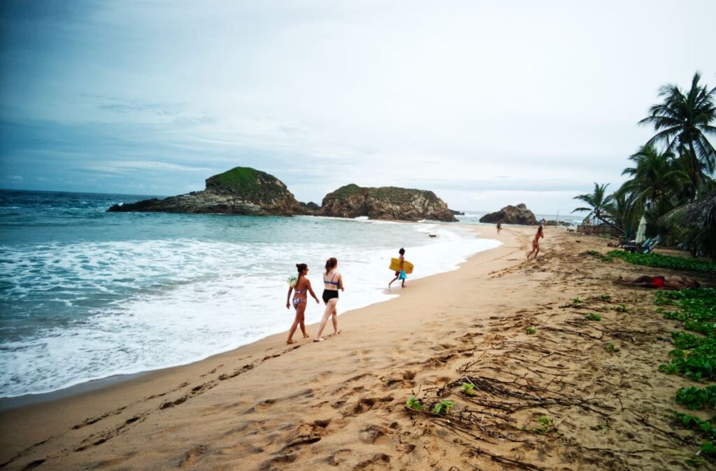 Swimmers and surfers walk along the ocean line among one of several open coves in San Agustinillo.