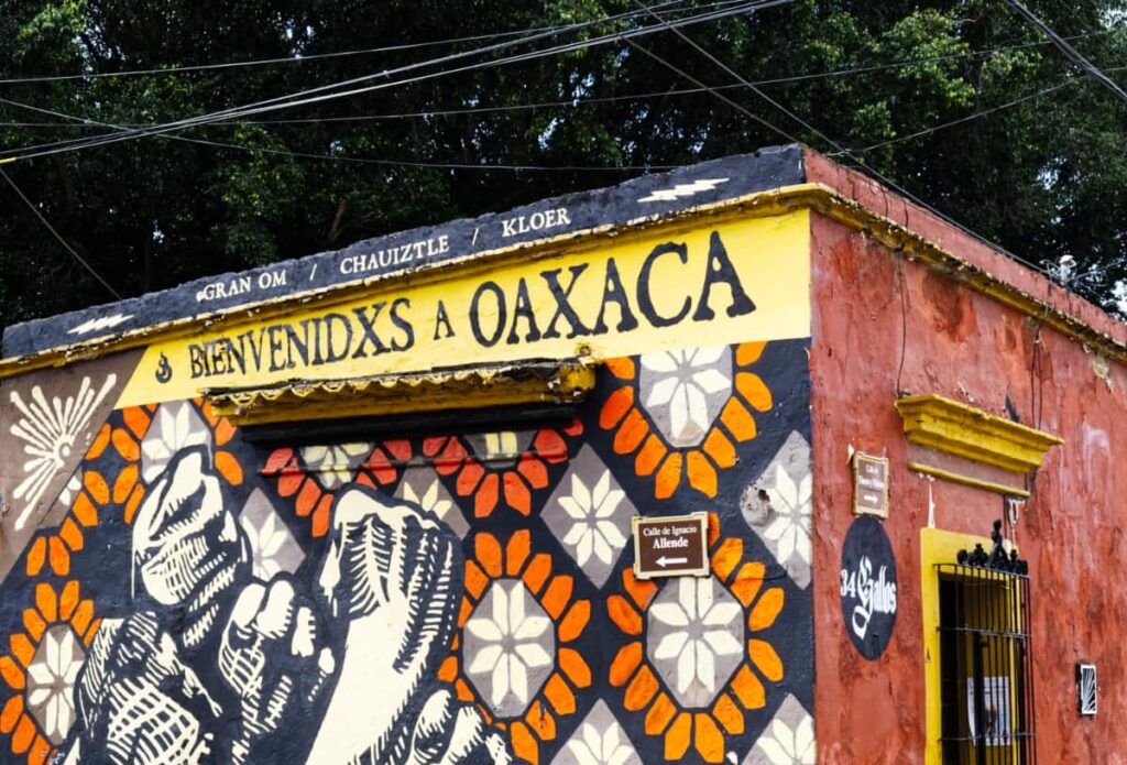 The outside of an art studio in Oaxaca is painted with a graphic design of fists in the area, uniting together. At the top reads, "Welcome to Oaxaca," in Spanish.