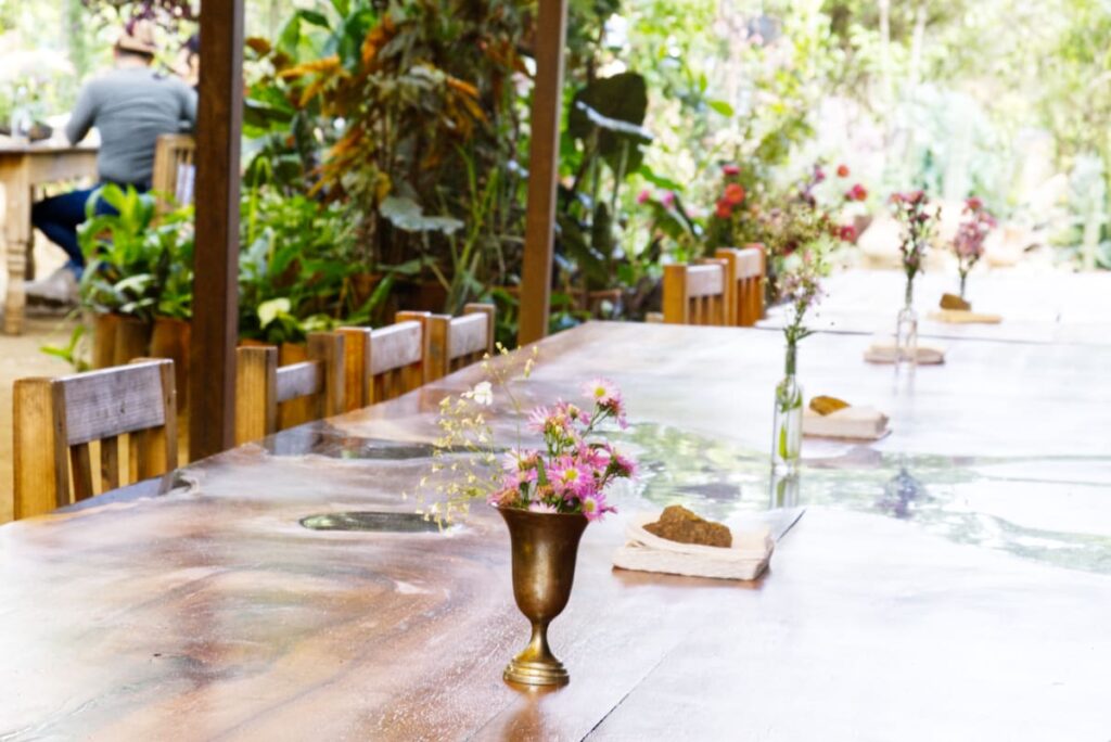 At Almu Restaurant, small vases of flowers sit on the large wooden table surrounded by plants.