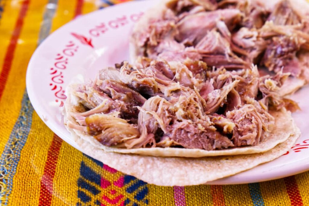 A plate of shredded barbacoa de borrego tacos sit on a colorful Mexican tablecloth.