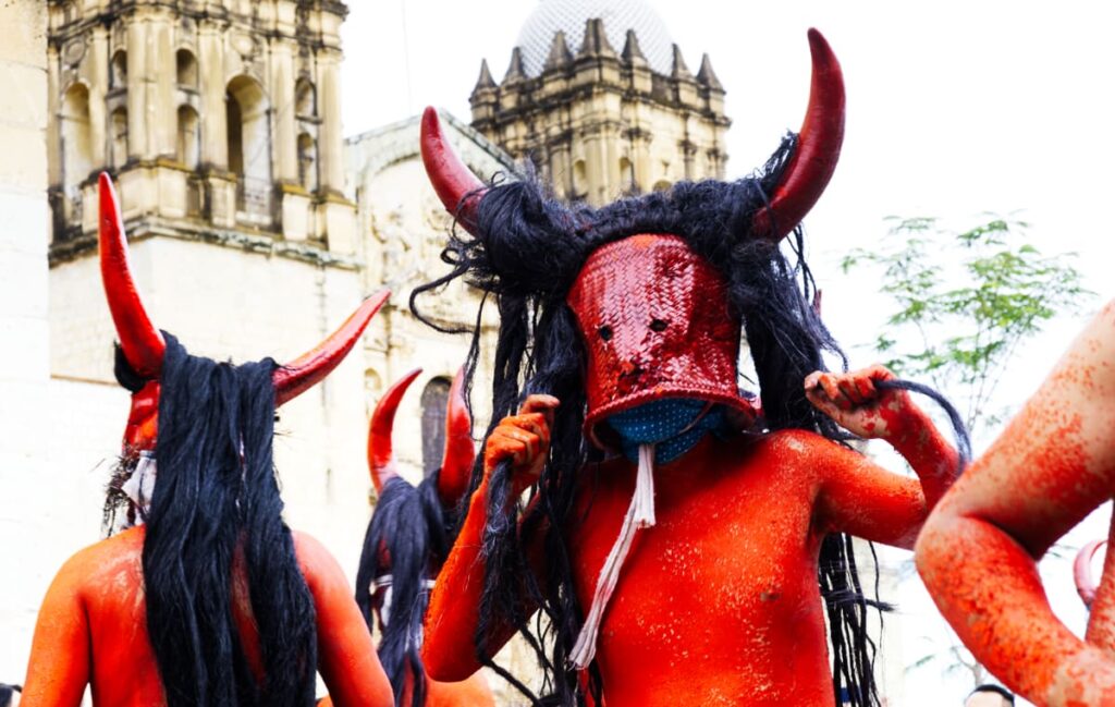 With their bodies painted red, men dress as los chachudos, or devils, for a Oaxaca festival in Santa Maria Coyotepec. Covering their faces is a mask made of a red painted baset. On their head are red horns and long black hair.