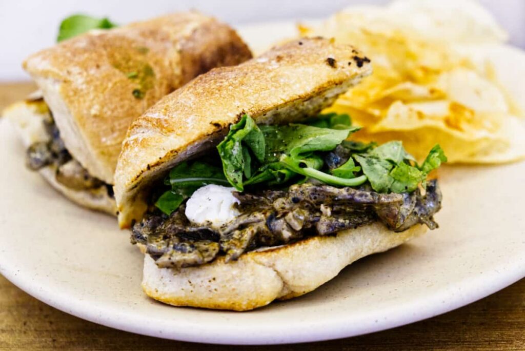 A sandwich of sauteed mushrooms, goat cheese, and greens on a baguette and served with chips at Onno Loncheria.