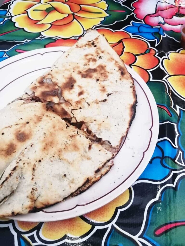 A large tortilla is stuffed with cheese and other ingredients and folded in half to form a tlayuda.