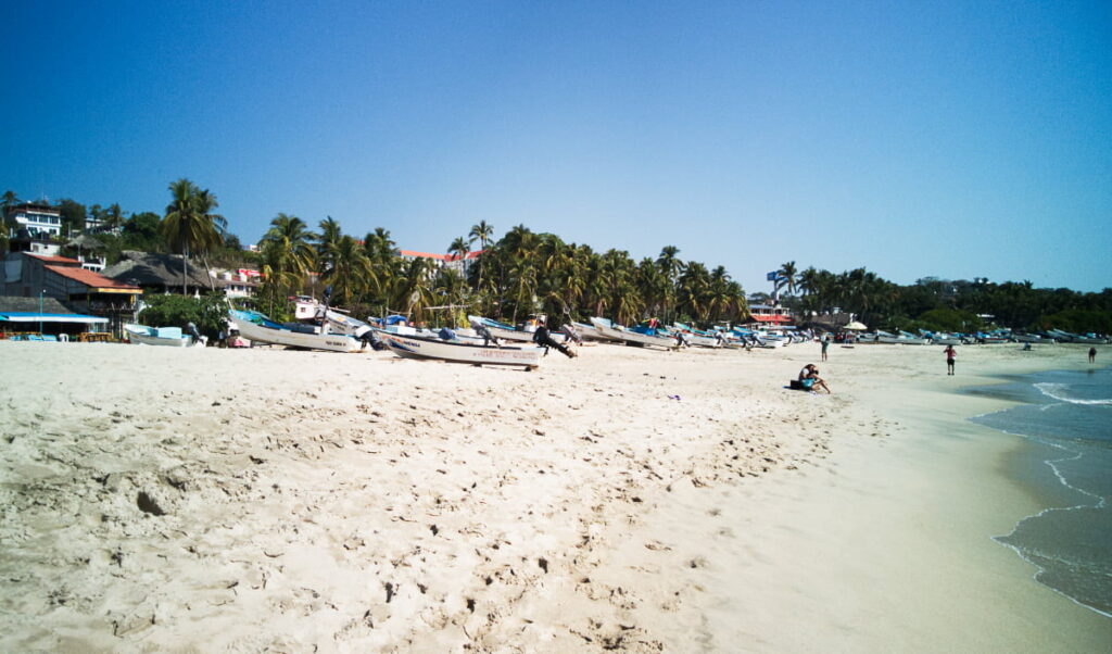 Boats and people sit in the sand in this wide shot of Bahia Principal, one of the main Puerto Escondido beaches.
