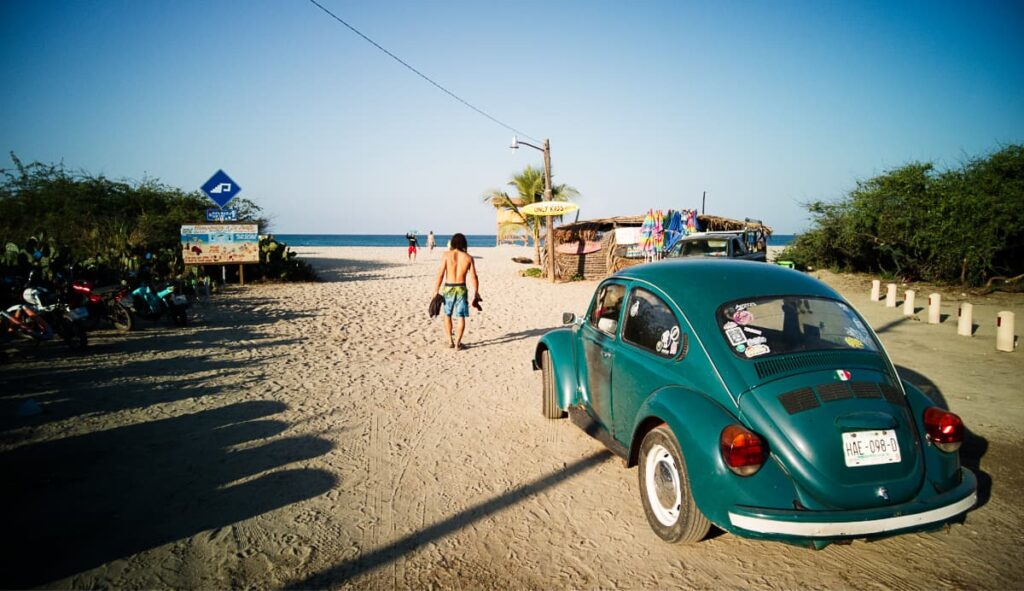 A man walks towards the beach in front of a bright green Volkswagen bug car in La Punta a place where to stay in Puerto Escondido.