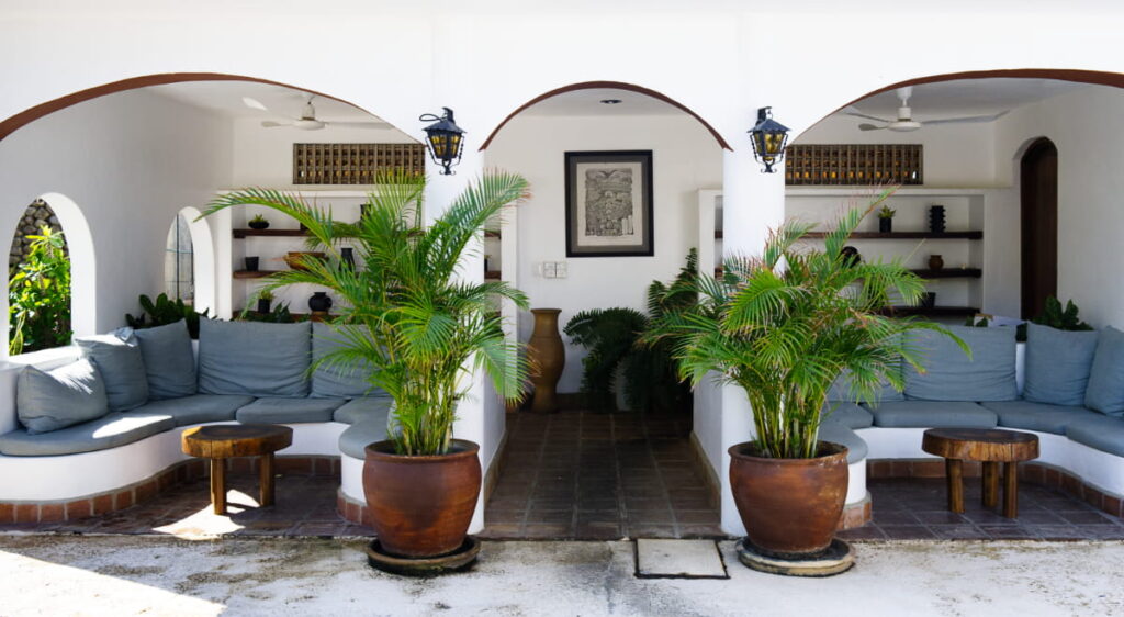 Grey cushions line the bench seating at Villas Carrizalillo, one of the best places to stay in Puerto Escondido. In front of the arched ceilings are two large clay planters with green tropical plants.