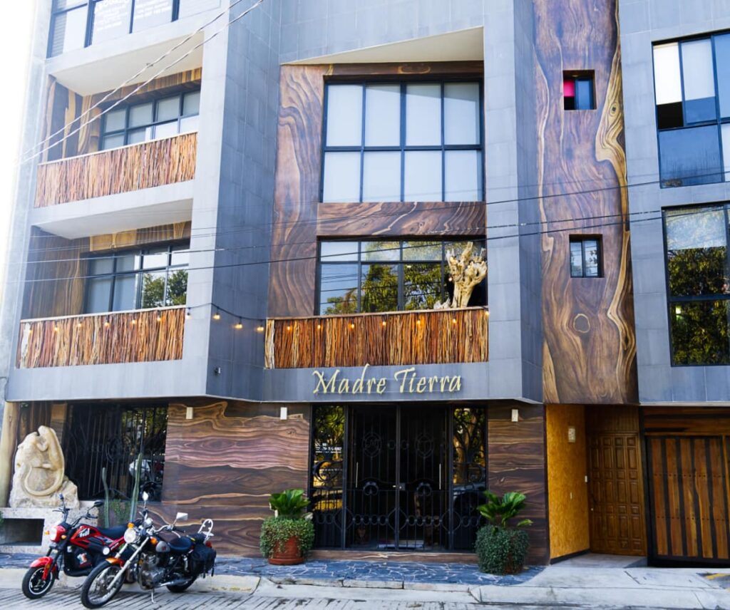 The outside of Madre Tierra Apartments, the answer of where to stay in Puerto Escondido, features large slabs of wood with grain patterns and lots of windows.