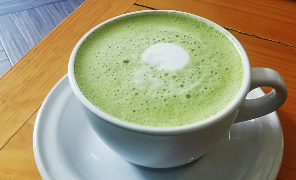 A match latte. Green liquid with foam and a few bubbles sits in a coffee mug.