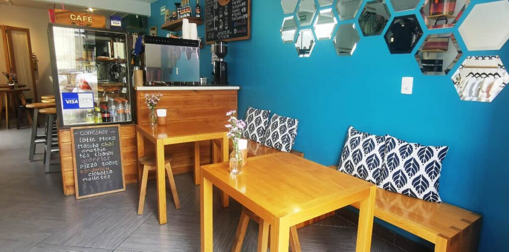 At Sorbo Cafe in Oaxaca, Centro, deep turquoise walls are balanced by light wood tables and chairs. The wall is decorated with at least a dozen honeycomb shaped mirrors. In the background in a hand written chalk menu and the coffee bar.