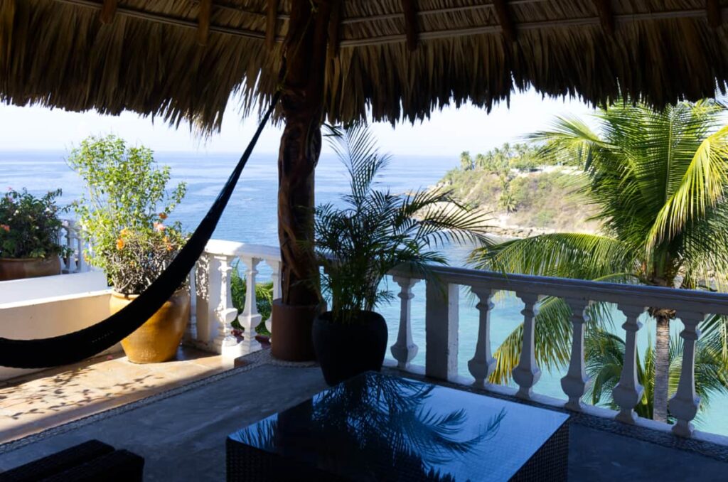 A hammock hangs under the palapa roof at Villas Carrizalillo. In the background is views of the open ocean.