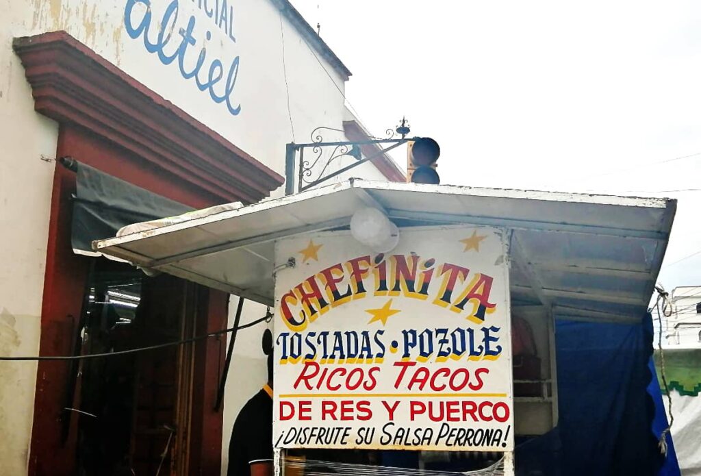 At Chefinita, one of the best tacos in Oaxaca, a white taco stand is painted with the words Chefinita, tostadas, pozole, ricos tacos in red, yellow, and blue.