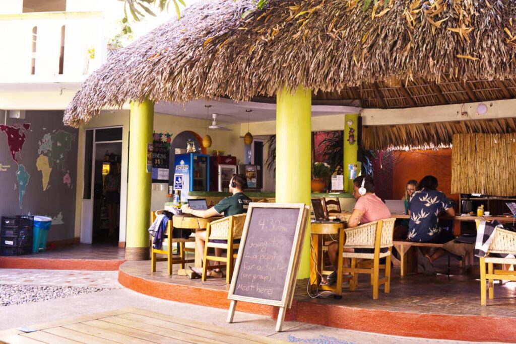 Several digital nomads work from their computers under the palapa at Casa Losodeli and Coworking in Rinconada. Two in the foreground are wearing headphones.