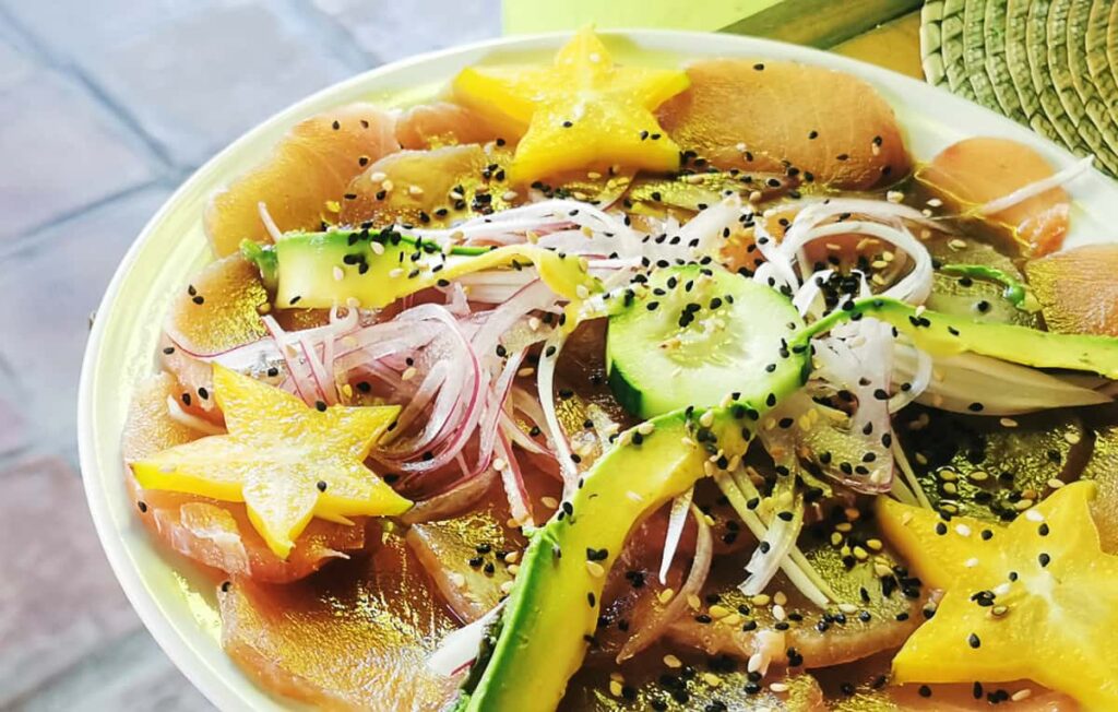 At La Salsa, one of the places for the best seafood in Puerto Escondido, a plate of fresh slices of fish is topped with a sauce, thin slices of red onion, avocado, cucumber, and decorate with pieces of star fruit.
