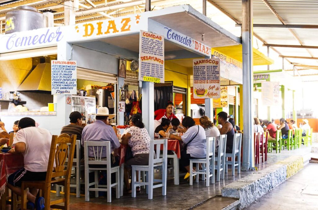 At the Puerto Escondido market, people sit at long tables in wooden chairs to eat breakfast. The hand painted signs hang above to advertise the seafood and breakfast available.