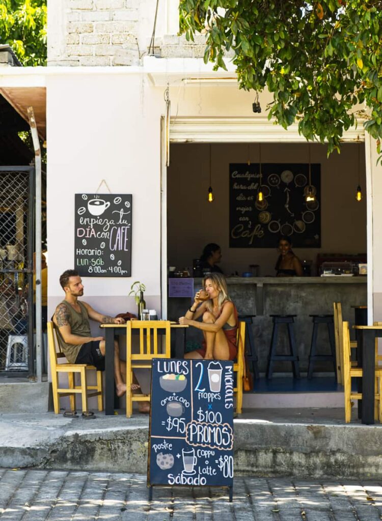 Two people sit outside of a cafe in Puerto Escondido. In front is a sign announcing the weekly promotions.