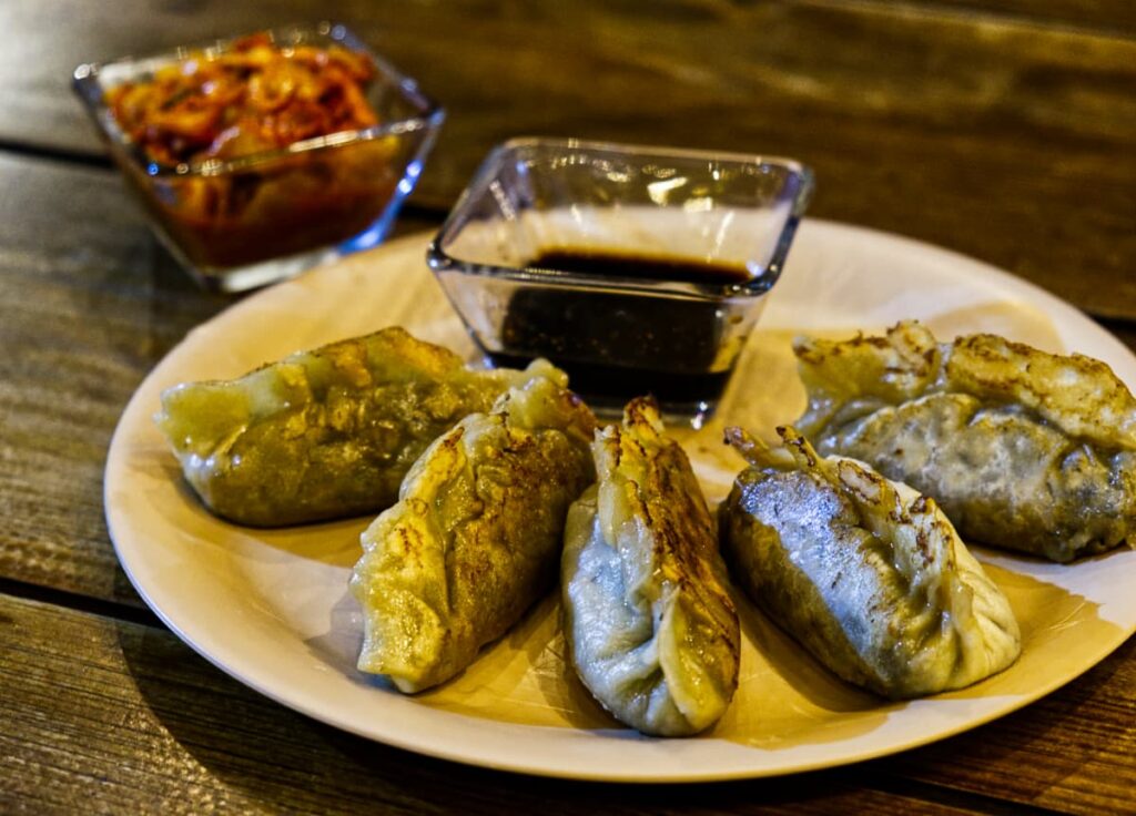 Give steamed vegan Korean dumplings circle a plate with a side of soy and kimchi.