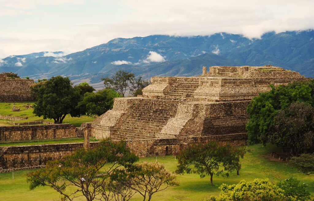 At Monte Alban, one of the top things to do in Oaxaca, a pyramid structure is surrounded by green trees and mountains.