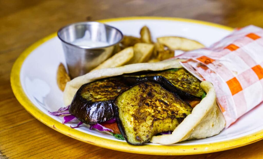 One of the vegan dishes at Nana Cafe in Oaxaca features large pieces of sauteed eggplant and fresh veggies wrapped in a thick pita. French fries and a sauce is served on the side of the place.