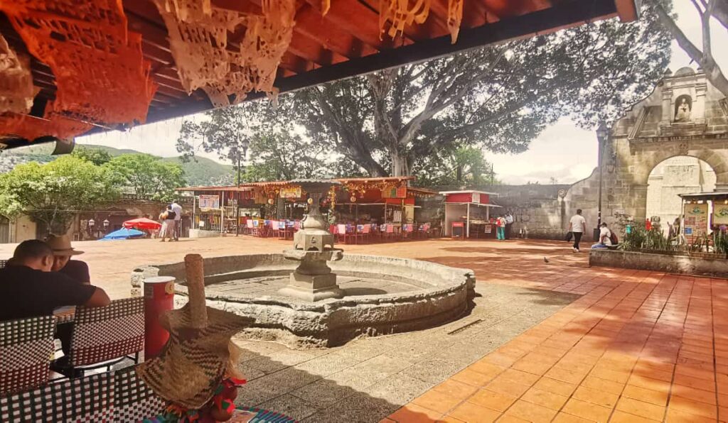 An open plaza surrounded by nieve stands with a large stone fountain in the center.