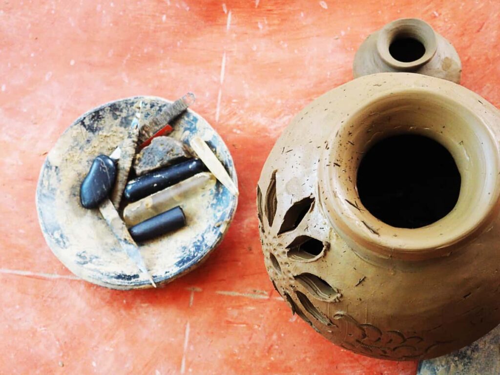 A carved clay pot sits on the floor next to a small dish of clay artisan tools at an artisan studio, one of the best things to do in Oaxaca.