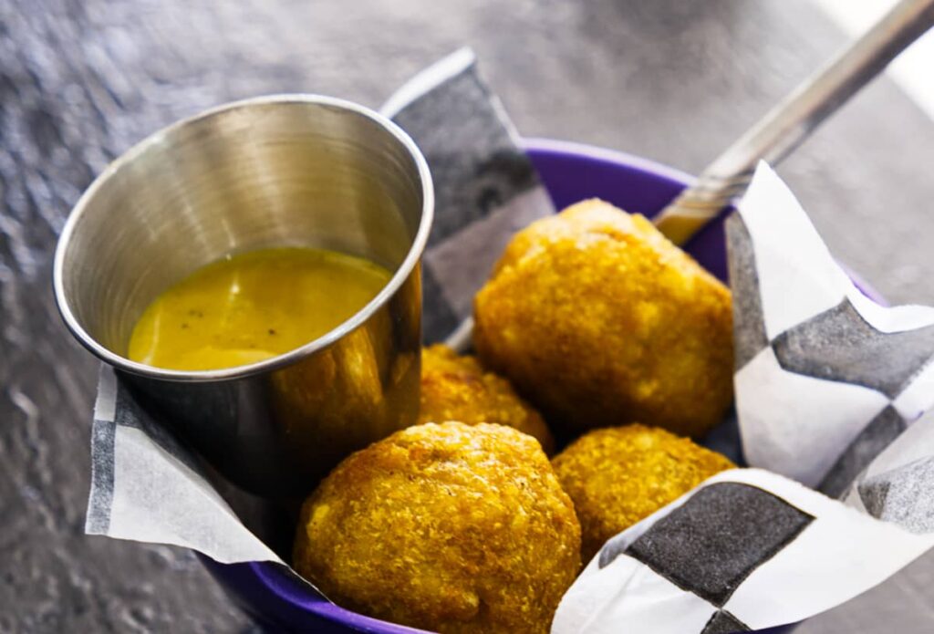 At PapaTots, a small bowl of fried vegan potato balls sits in a bowl with a side of yellow sauce