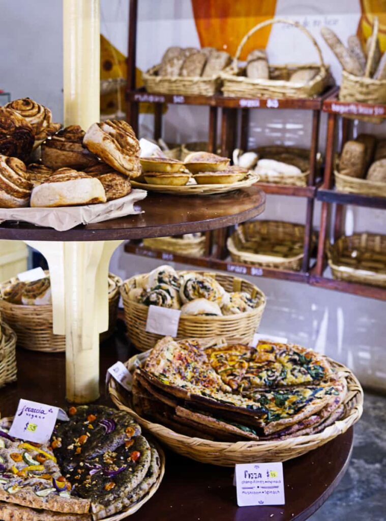 At Canastas, a bakery in Mazunte, baked goods sit in baskets on a two tiered table. On the wall in the back, more baskets filled with fresh baked bread line the shelves.