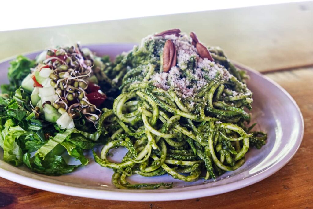 A plate of zucchini noodles topped with cheese and pecans is served with a side salad featuring sprouted beans at Luz del Sol, the original vegetarian restaurant in Mazunte.