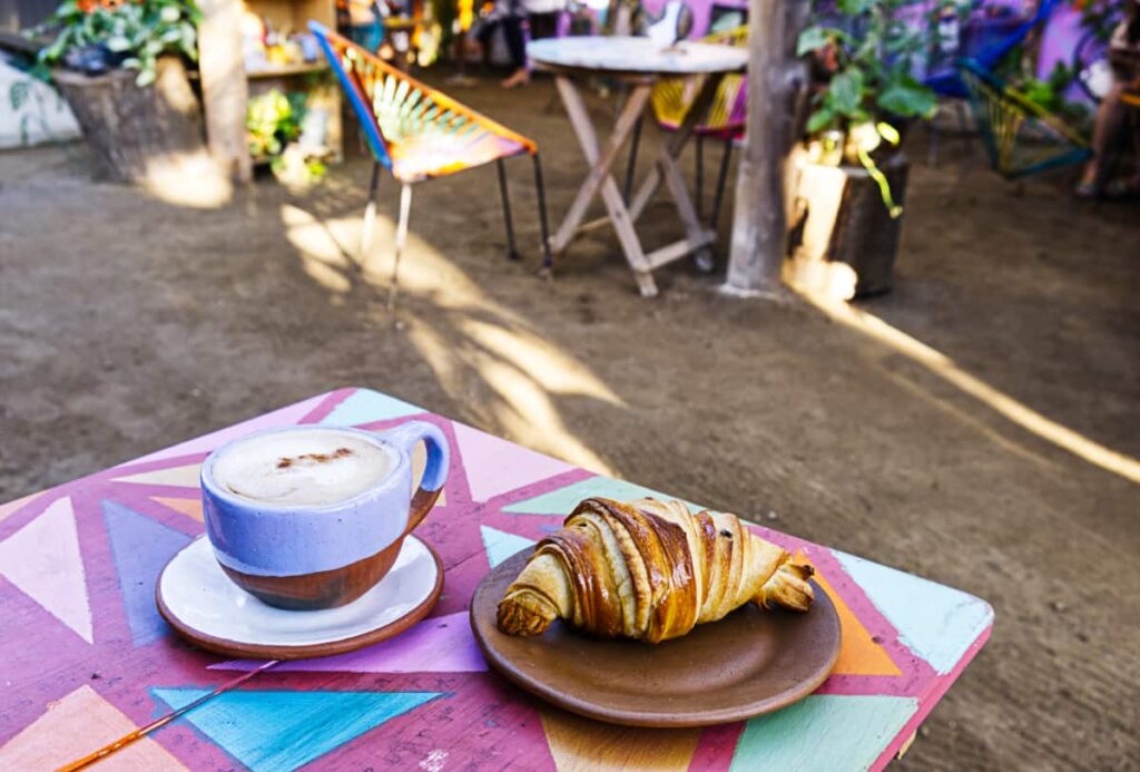 On a colorful table at one of the bakeries in Mazunte, a fresh baked croissant sits on a clay plate next to a hot cappuccino.