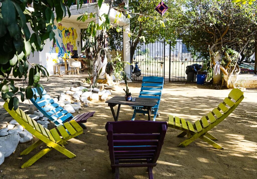 Several colorful wooden chairs sit in a circle around a table in the garden area at El Mundito Coliving, Puerto Escondido.
