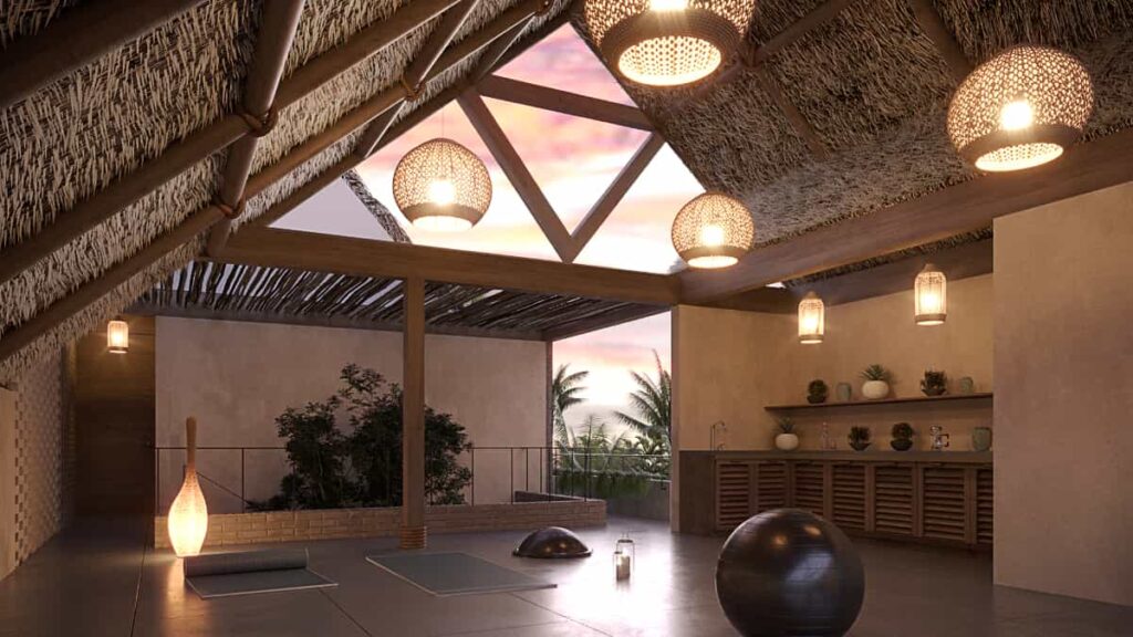 The terraza wellness space at SobreLuna coliving in La Punta features a wide-open room with sky views that face the ocean in this 3D render. From the natural materials that create the roof hang several lights. On the floor are yoga mats and an exercise ball.