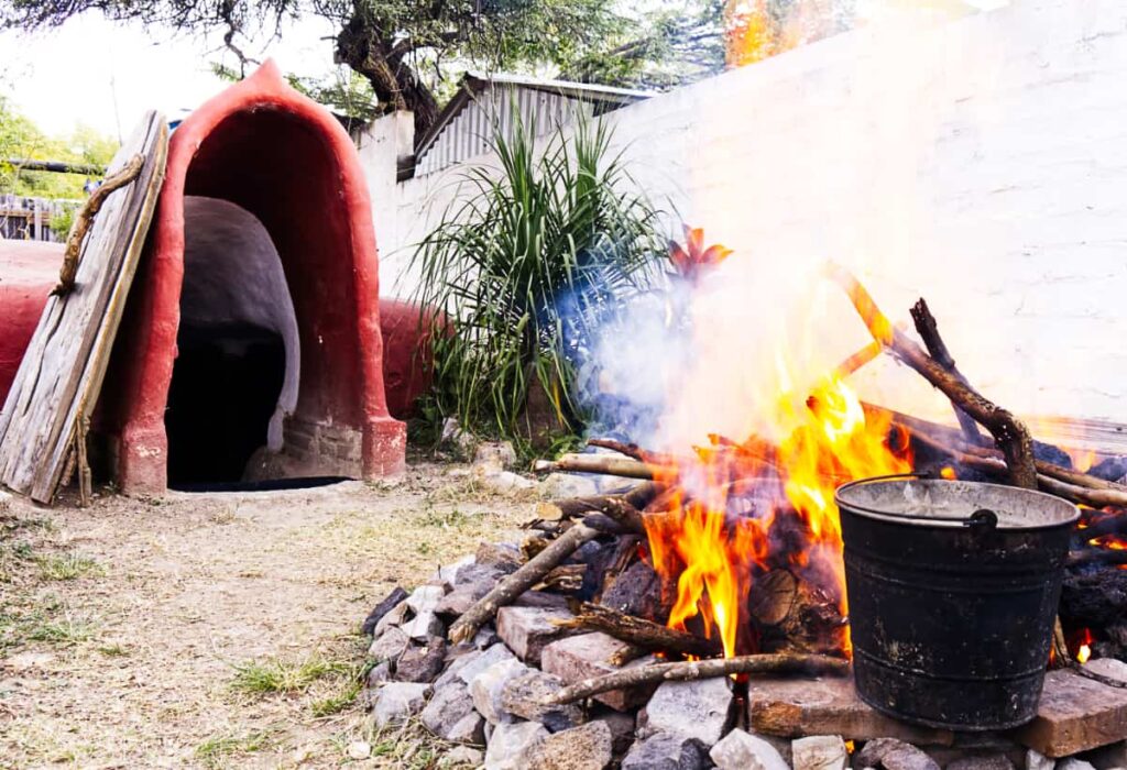 The opening to the best temazcal in Oaxaca while in front, a fire heats the stones used during the ceremony. A black bucket of water sits in front.