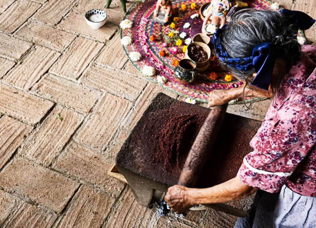 An overhead view of the grandmother grinding cacao on a stone metate before a Oaxaca temazcal ceremony.