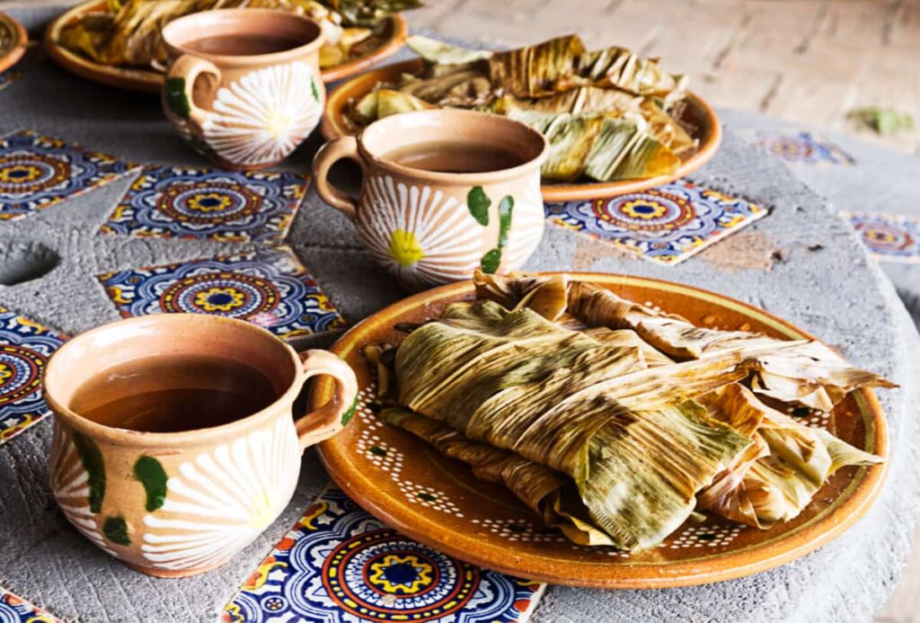 Three plates of corn leaf tamales and cups of herbal tea sit on a table after a temazcal ceremony.