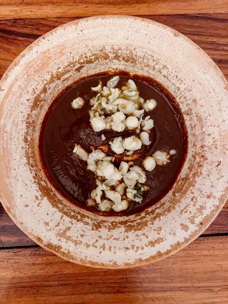 An overhead shot of a plate of mole coloradito. The thick, dark red sauce covers a piece of chicken and is topped with pieces of corn.