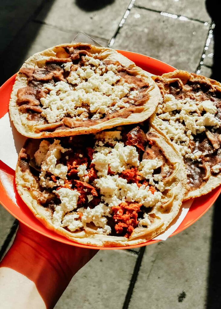 A plate of three memelas, a typical food of Oaxaca, They are topped with a thin bean paste, fresh crumbled cheese and chorizo.