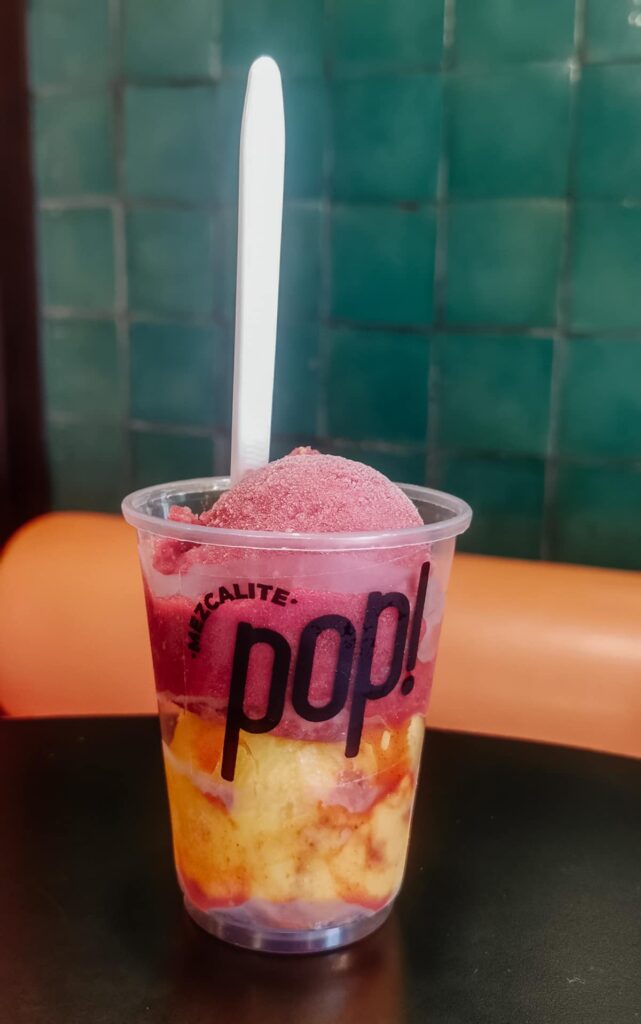 Two flavors of brightly colored mezcal sorbet are layered in a plastic cup from Mezcalite Pop!