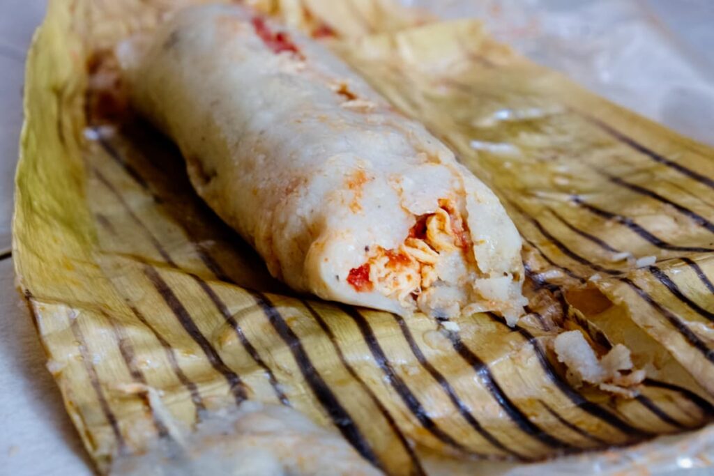A Oaxacan tamale sits on top of the banana leaf in which it was cooked in. The tamale consists of chicken and sauce enveloped in a corn dough.