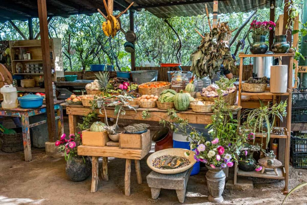 Baskets of fresh produce and other ingredients sit on a large wooden table at Almu restaurant in San Martin Tilcajete, Oaxaca. Above the table hangs bananas and a large pile of avocado leaves, an ingredient used in traditional Oaxacan food.