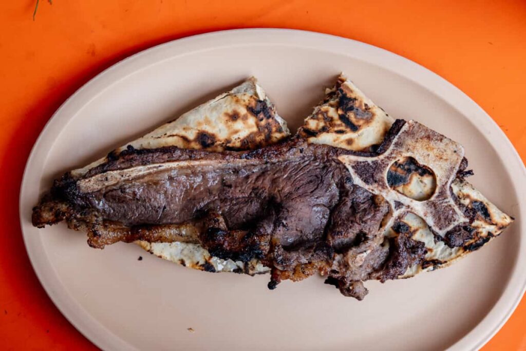 A mini tlayuda in Oaxaca topped with a thin beef ribeye on the bone that covers the entire tlayuda.