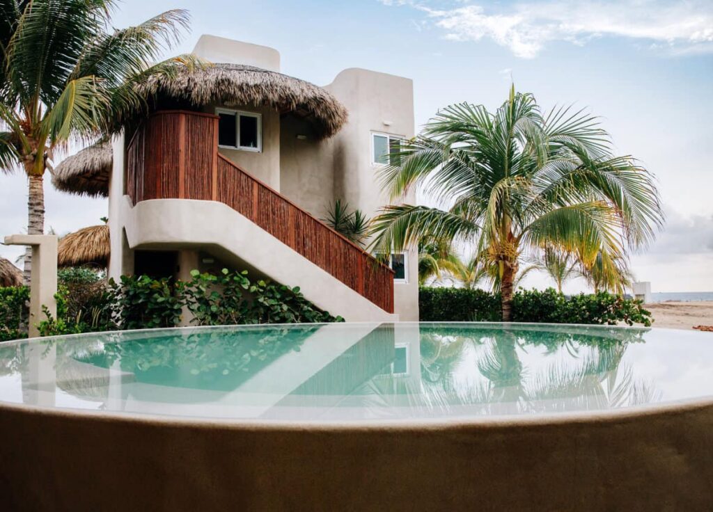 A view of deluxe bungalow at El Origen Villas & Spa with outdoor pool, lush greenery and palm trees.