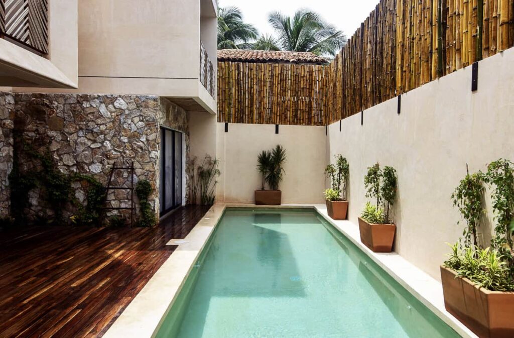 A view of a private pool at Casa Ita Surf furnished with potted plants, wooden flooring and a whitewashed wall.